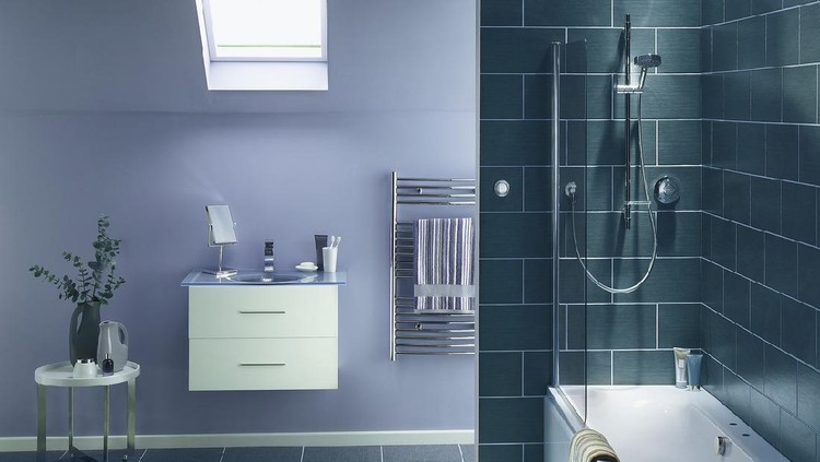 The interior of a simple, modern bathroom in a , cool, blue-gray tone. There is a sink, mirror,bath and shower, a hand towel holder. There are dark rectangular tiles on the wall, and lighter gray tiles on the floor.