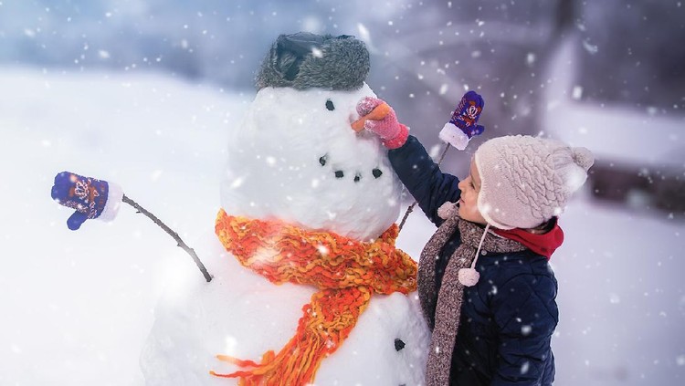Child sculpts a snowman in a park