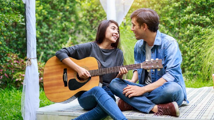 Ilustrasi Lagu Cinta Young Asian loving couple playing guitar in the park, outdoors