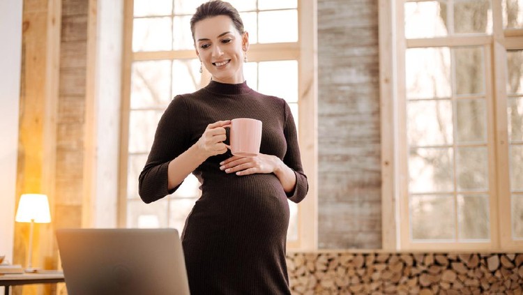 Tea time. Appealing pensive pregnant businesswoman holding cup while looking down and standing