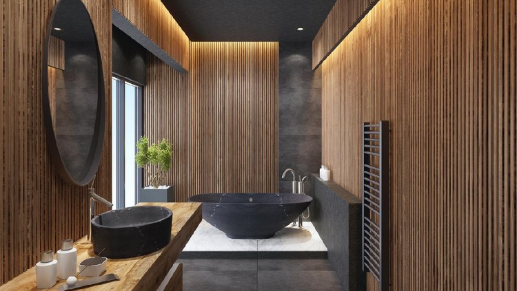 contemporary minimalist bathroom with wooden walls. 

oval mirror with black frame is on the wall with wooden battens.

round stone washbasin and inox basin tap is on top of the long wooden 

vanity unit. freestanding black stone bathtub and floor mounted inox tap

is on a platform with large white marble tiles. grey wall shelf and grey towel 

radiator on wooden wall. black ceiling with strip cove lighting with embedded spotlights.