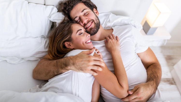 Beautiful loving couple kissing in bed. beautiful young couple lying together on the bed. Romantic young couple in love lying on bed. Beautiful couple smiling in bed.