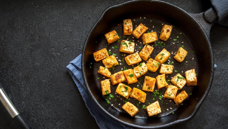 Ilustrasi Tahu Renyah Fried tofu with sesame seeds and spices on cast iron pan, copy space. Healthy ingredient for cooking vegan vegetarian diet food. Roasted tofu over black background.