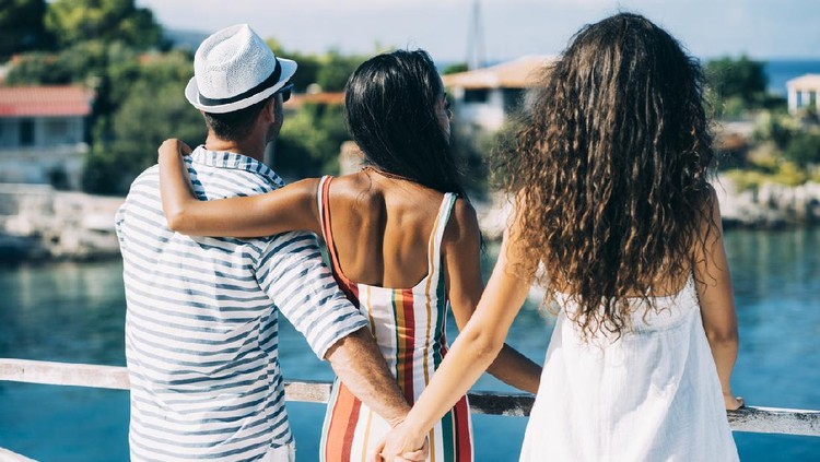 Couple in vacations standing on harbor, man hoding other woman's hand.