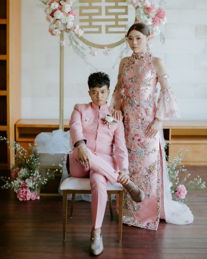 Ini dia penampilan Reza dan Wendy dalam prosesi Tea Pai. Kompak mengenakan busana khas Tionghoa bernuansa soft pink, gaun Wendy yang bermodel halterneck tampak elegan dengan detail payet dan lengan lonceng. (Foto: instagram.com/baliweddingspecialist)