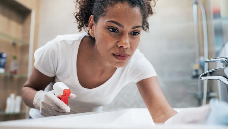 Woman cleaning with spray disinfectant and gloves in the bathroom at home