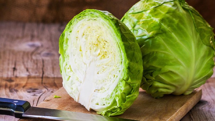 Fresh green cabbage cross section with water drops on rustic wooden cutting board, kitchen knife in forground. Close up, selective focus