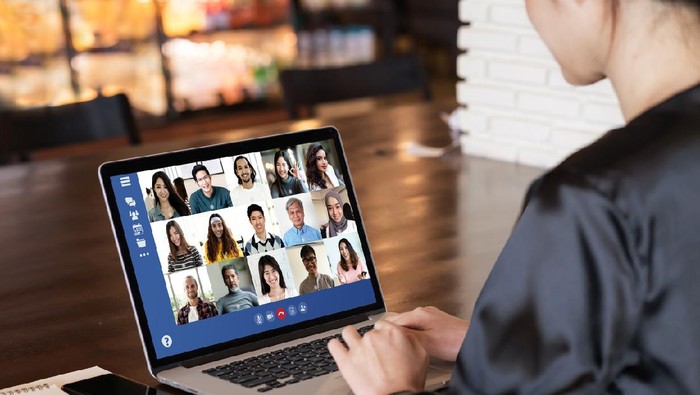 View over businesslady shoulder seated at workplace desk look at computer screen where collage of many diverse people involved at video conference negotiations activity, modern app tech usage concept