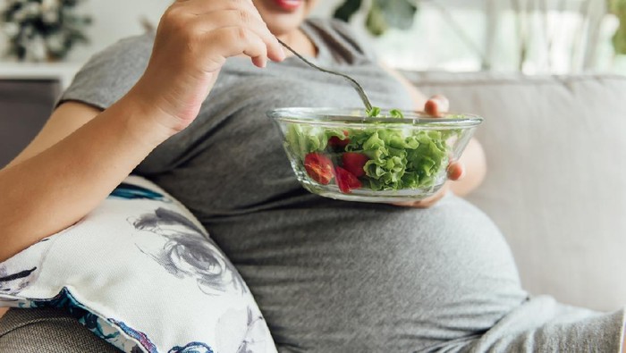 An Asian pregnant woman is eating green vegetables