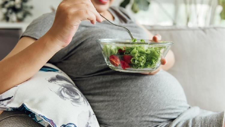 An Asian pregnant woman is eating green vegetables