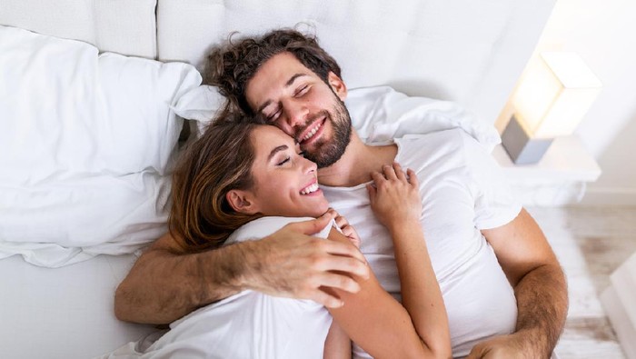 Beautiful loving couple kissing in bed. beautiful young couple lying together on the bed. Romantic young couple in love lying on bed. Beautiful couple smiling in bed.