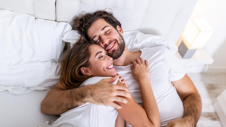 Beautiful loving couple kissing in bed. beautiful young couple lying together on the bed. Romantic young couple in love lying on bed. Beautiful couple smiling in bed.