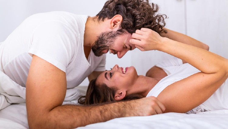 Affectionate young attractive couple sharing a romantic moment in the bedroom at home. Happy young couple hugging and smiling while lying on the bed in a bedroom at home.