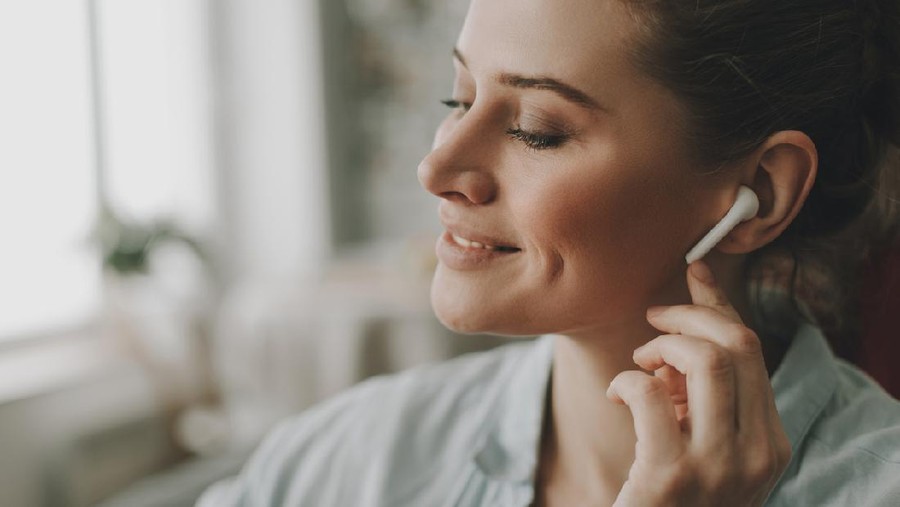 earphone Technology in our life. Close up portrait of young relaxed woman on sofa enjoying of music via wireless earbuds at home