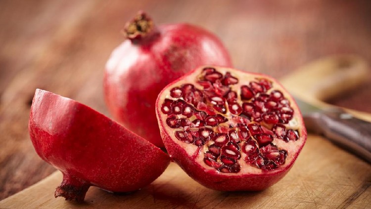 Buah Delima Sliced pomegranate on cutting board with knife and whole pomegranate behind. Shot with shallow focus on sliced fruit.