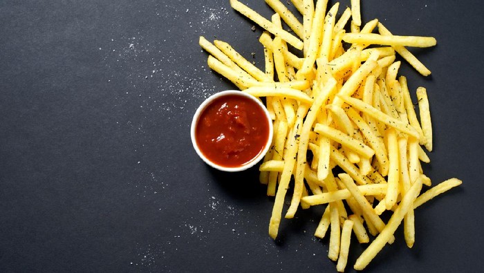 French fries with tomato sauce on a black background.