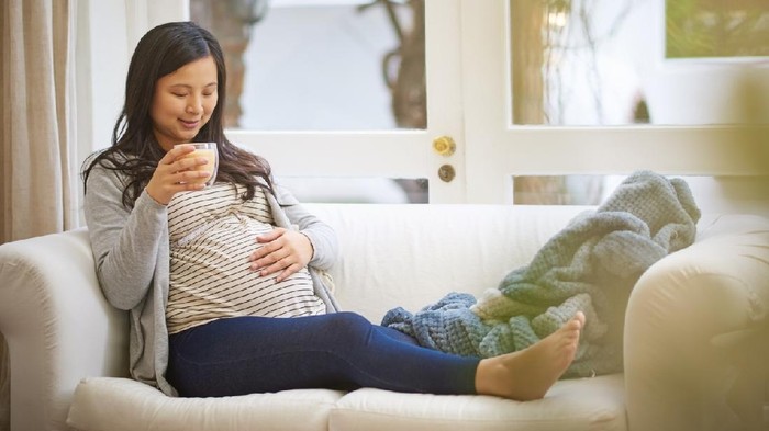 Shot of an attractive young pregnant woman drinking an iced coffee while relaxing on the sofa at home