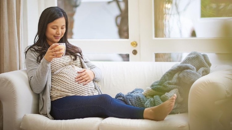 Shot of an attractive young pregnant woman drinking an iced coffee while relaxing on the sofa at home
