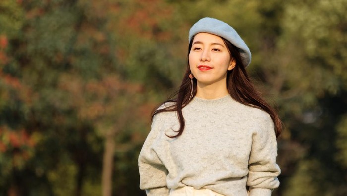 Portrait of beautiful Chinese young woman in woolen sweater and blue beret smiling with hands in pocket, charming Chinese girl with black long hair enjoy her leisure time outdoor.
