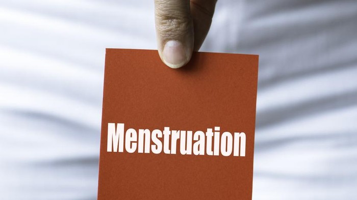 Torso of an unrecognizable woman is showing red square card to camera representing with menstruation written in white.
