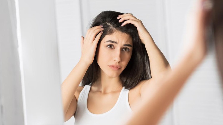 Portrait of a beautiful young woman examining her scalp and hair in front of the mirror, hair roots, color, grey hair, hair loss or dry scalp problem