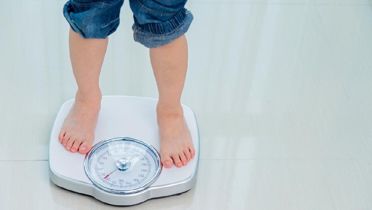 Ilustrasi berat badan anak Boy measures weight on a weight scale.