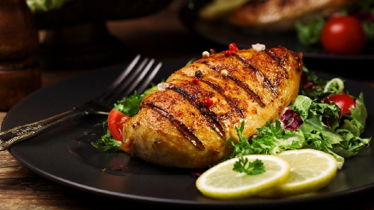 grilled chicken breast with green salad and french fries on a black plate.