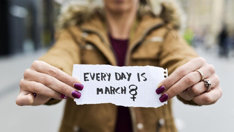 closeup of a young caucasian woman in the street showing a piece of paper with the text every day is march 8 written in it