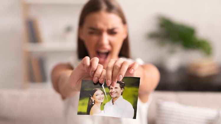Breakup. Furious Woman Ripping Wedding Photo With Ex-Husband Sitting On Sofa Indoor After Divorce. Selective Focus