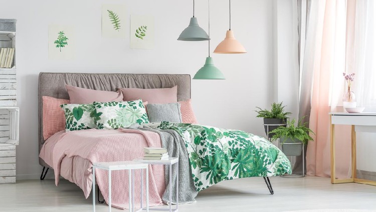 Pastel beddings on stylish bed in white bedroom with plants