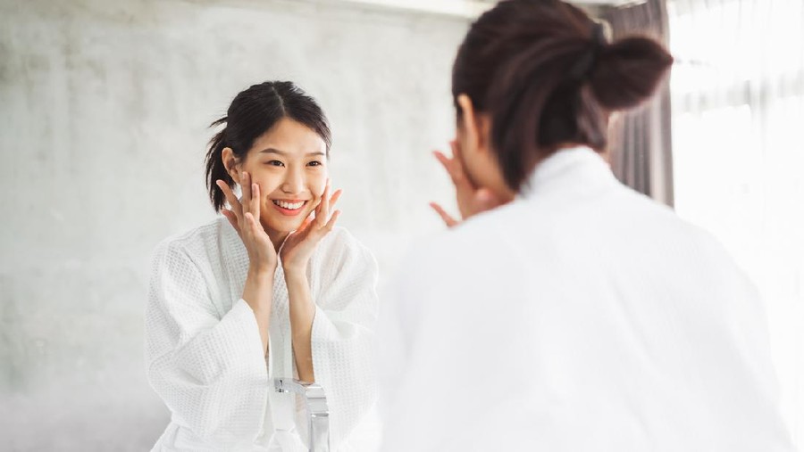 Asian woman cleaning face front of mirror&comma; skin care and cosmetic removal concept