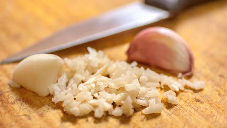 Bawang Putih Cincang Garlic chopped over a wooden cutting board on a kitchen