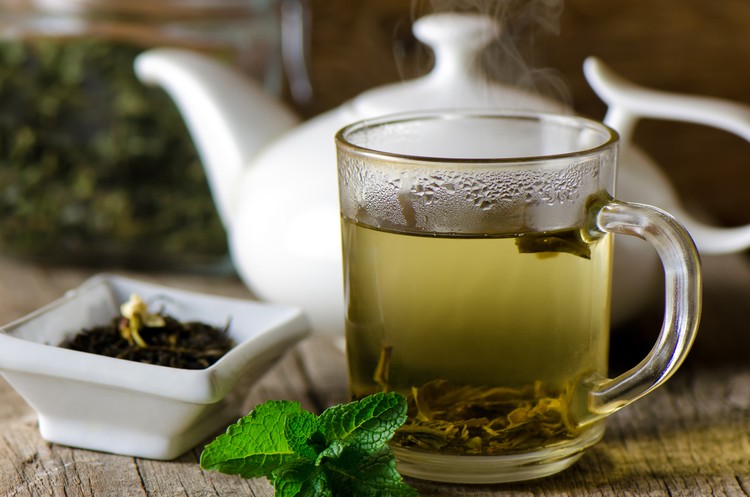 Ekstrak Teh Hijau Glass cup with fresh green tea and mint.