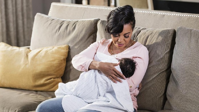 A mid adult African-American woman in her 30s nursing her 2 month old baby boy, looking down at him, lovingly. The child is bundled in a blanket.