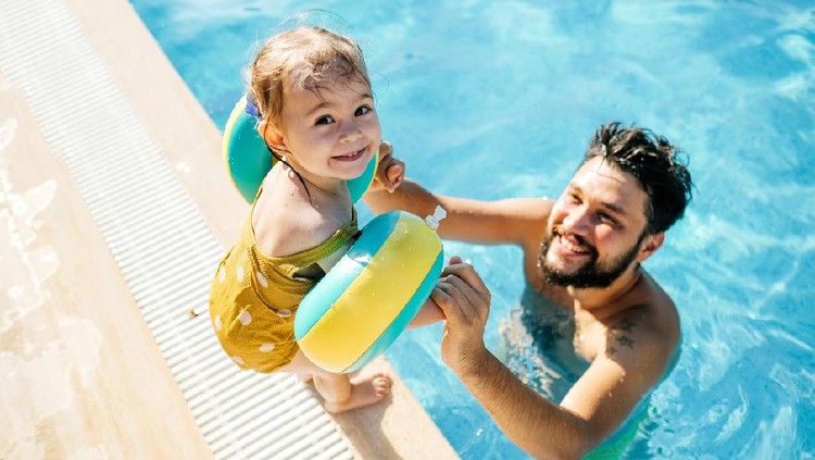 Cute little girl having fun with parents in pool