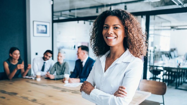 Shot of a beautiful african-american businesswoman standing with arms crossed in front of her team in board room. Multi-ethnic group of business people on meeting in conference room.
