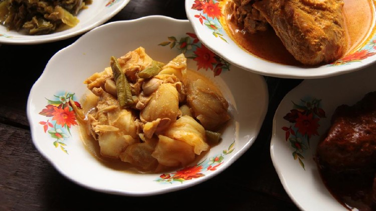 Sayur Gulai Nangka, the popular vegetable dish of jackfruit in yellow curry. Plated in a small ceramic plate and served among many other Minang side dishes in style typical to Minang eateries, plates stacking.