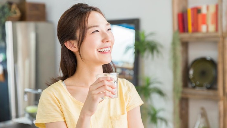1143177497 young attractive asian woman who drinks water in a kitchen