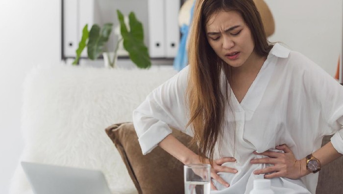 Asian beautiful women feel menstrual cramps and stomachache after menstruation.Hand holding stomach and belly after taking a medication.Problem and disorder of female body.