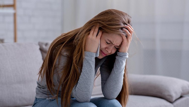 Sad young woman having conversation on mobile phone and crying at home. Millennial lady having difficult talk, hearing sad news, going through breakup or relationship problems