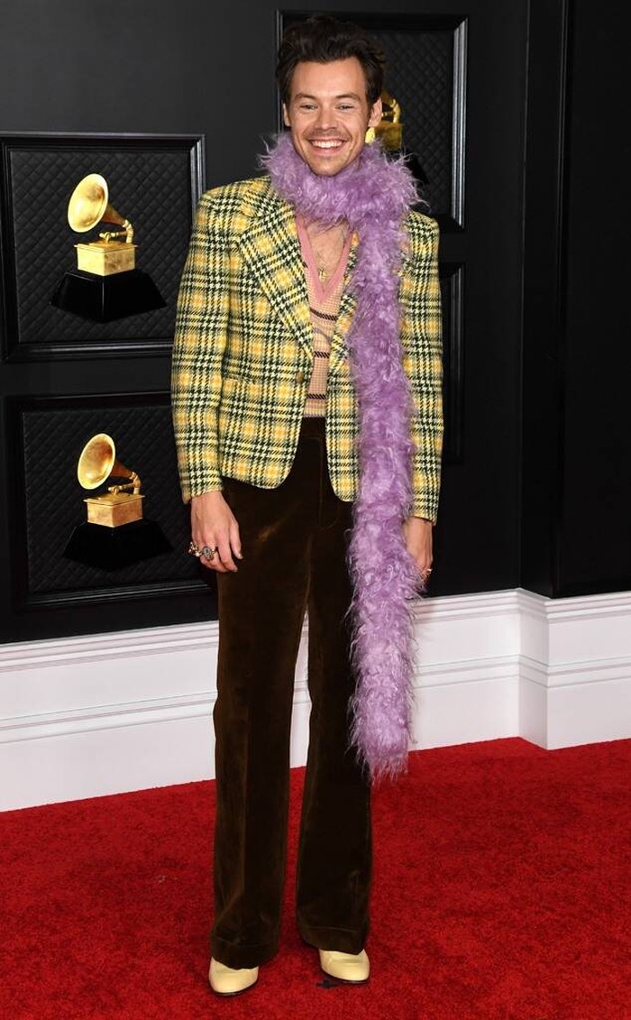 Harry Style hadir dengan penampilan yang terinspirasi dari fesyen era 90-an dalam red carpet kali ini dari koleksi Gucci. Dia memakai blazer motif kotak kuning-coklat, celana coklat dengan poin boa (selendang bulu) warna lilac/Sumber/E Online.