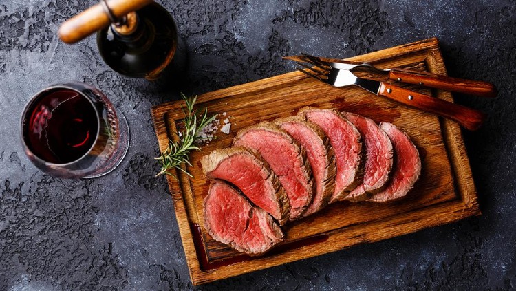 Sliced grilled tenderloin Steak roastbeef on wooden cutting board and Red wine on dark background