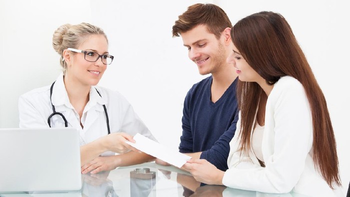 Female doctor giving prescription paper to couple at desk in clinic