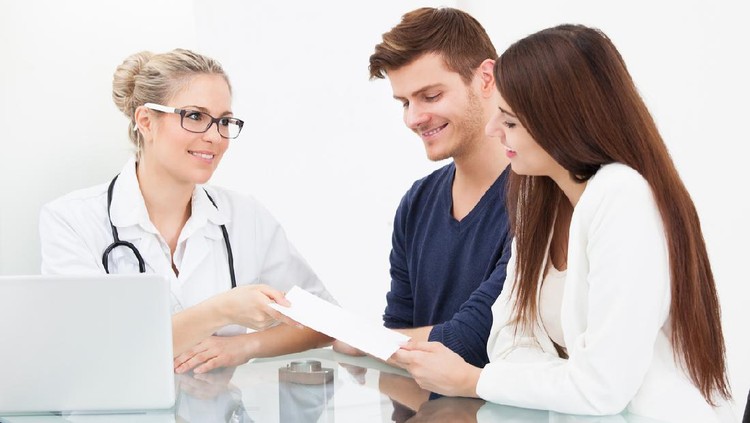 Female doctor giving prescription paper to couple at desk in clinic