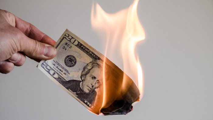 Hand holding a burning twenty US dollar bill on a white background
