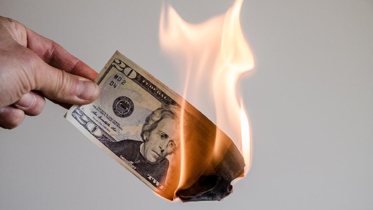 Membakar Uang Hand holding a burning twenty US dollar bill on a white background