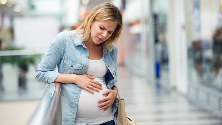 Pregnant woman in white t-shirt and denim shirt touching her belly, having pains