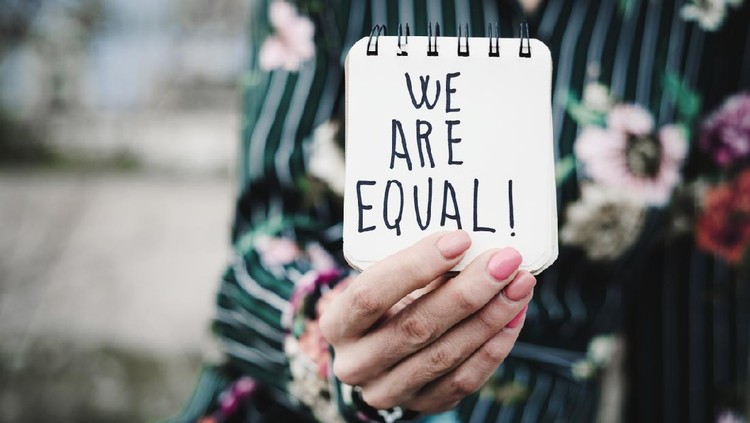 Ilustrasi feminis closeup of a young woman outdoors showing a notepad in front of her with the text we are equal written in it