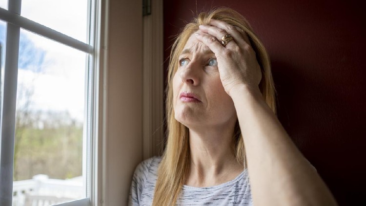 A depressed 47 year old woman stares out of a window about to cry during a pandemic that has her quarantined in her home.
