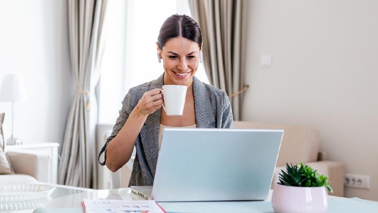 Business Women at home during pandemic isolation working on laptop and drinking coffee.Image of young pleased happy cheerful cute beautiful business woman sit indoors in office using laptop computer